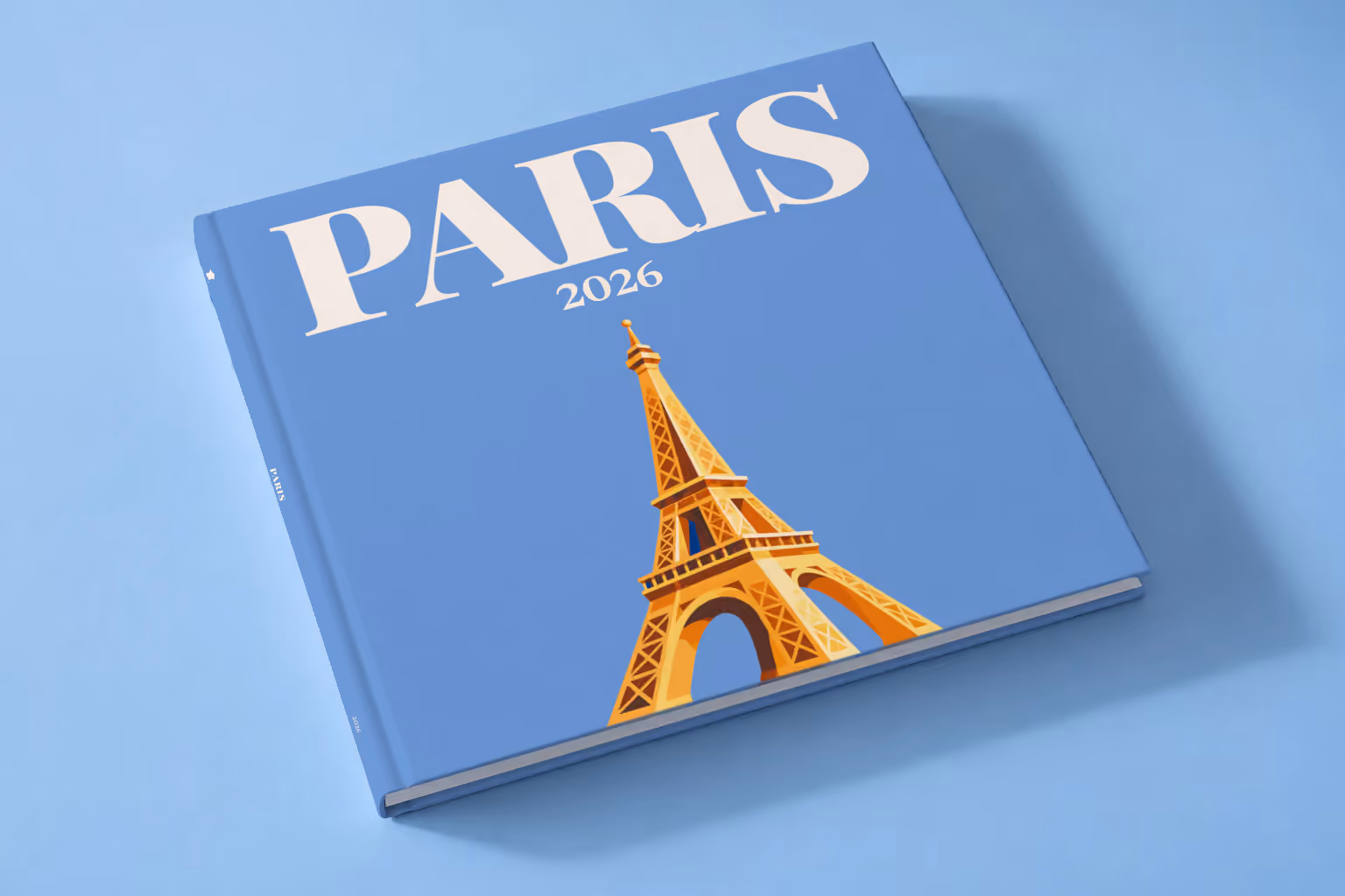 Paris square hardcover photo book with the illustrated cover of a gold Eiffel Tower on blue, lying on a pale blue studio backdrop