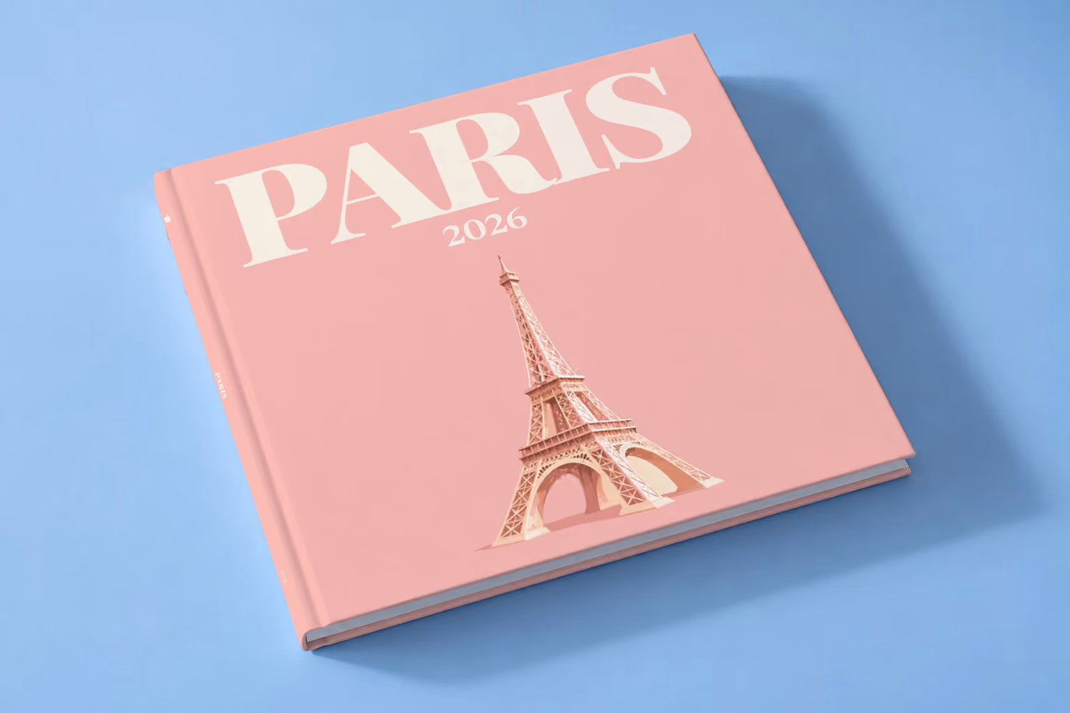 Paris square hardcover photo book with the illustrated cover of the Eiffel Tower on blush pink, lying on a pale blue studio backdrop