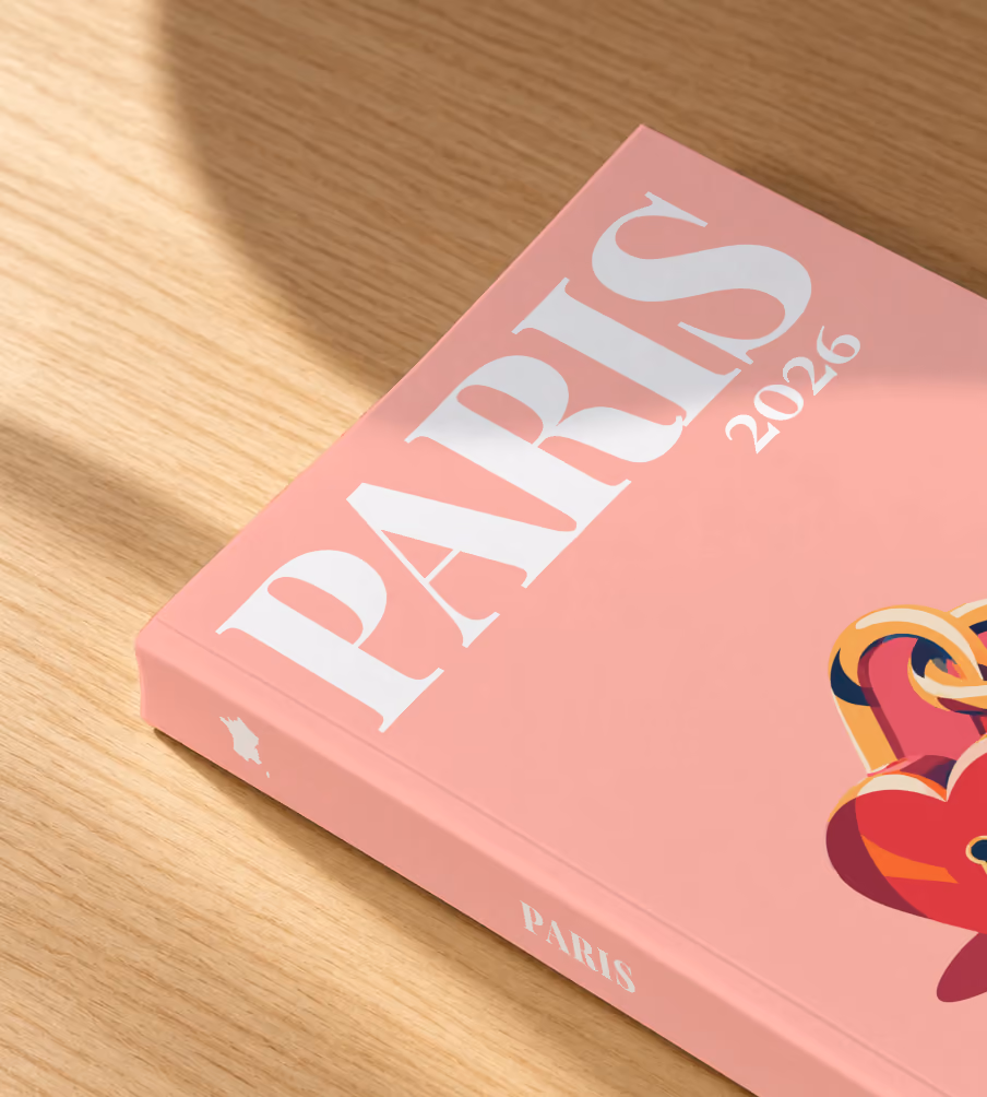 Paris softcover photo book with the illustrated cover of heart-shaped love locks on salmon pink, lying on an oak desk in dappled afternoon sunlight