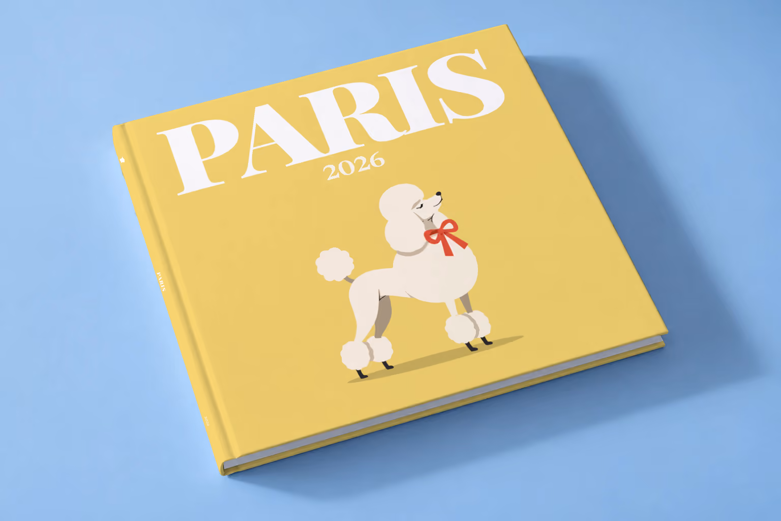 Paris square hardcover photo book with the illustrated cover of a white poodle with a red bow on yellow, lying on a pale blue studio backdrop