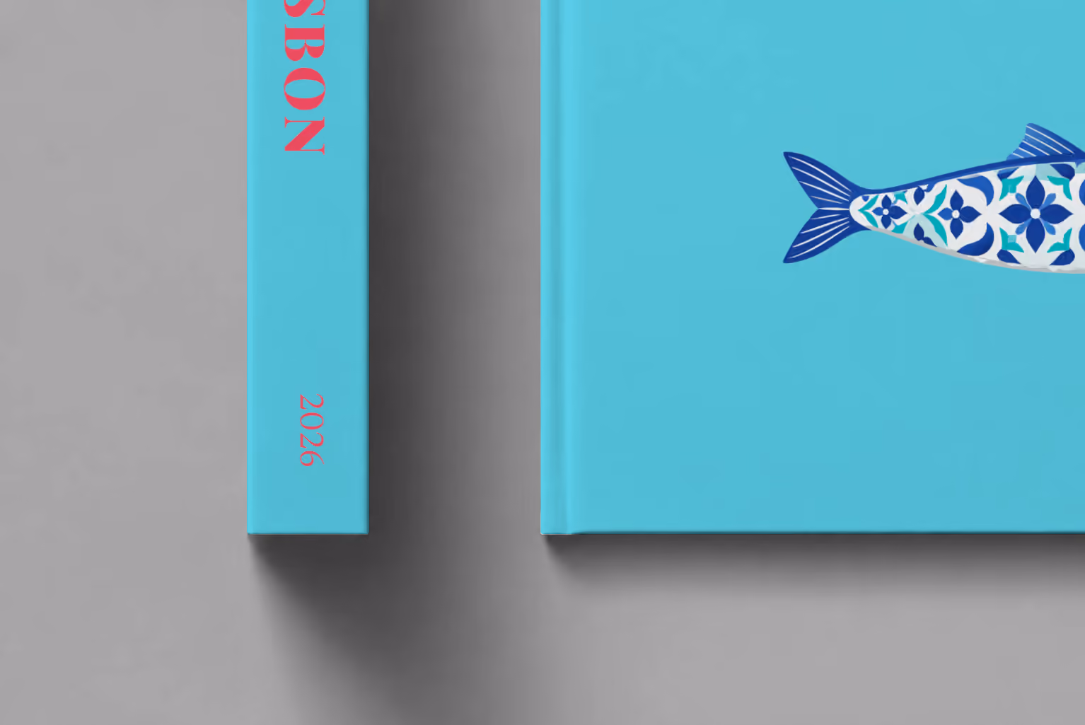 Portugal hardcover photo book with the Lisbon illustrated cover of a blue azulejo-tiled Portuguese sardine on turquoise, shown close up beside its spine on a pale grey studio surface