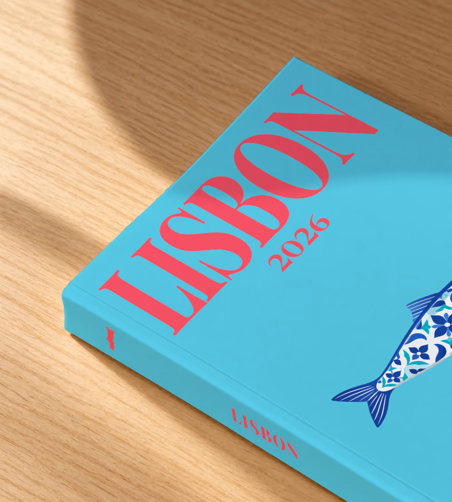 Portugal softcover photo book with the Lisbon illustrated cover of a blue azulejo-tiled Portuguese sardine on turquoise, lying on an oak desk in dappled afternoon sunlight