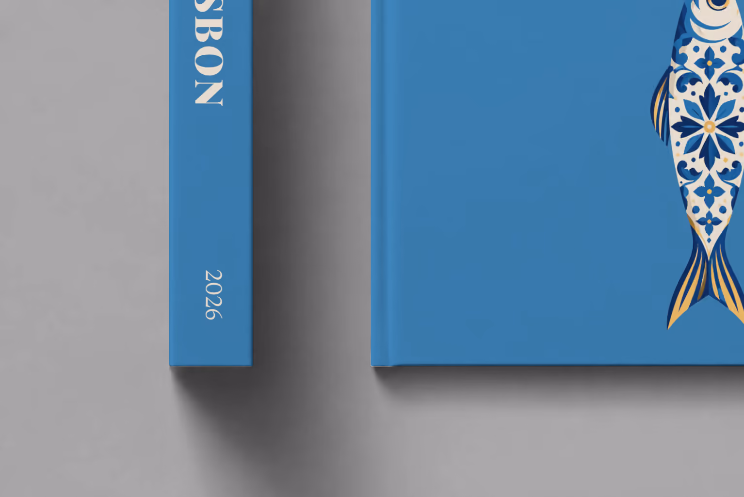 Portugal hardcover photo book with the Lisbon illustrated cover of a blue and white azulejo-tiled sardine on denim blue, shown close up beside its spine on a pale grey studio surface