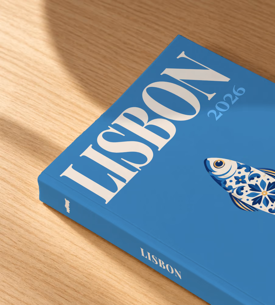 Portugal softcover photo book with the Lisbon illustrated cover of a blue and white azulejo-tiled sardine on denim blue, lying on an oak desk in dappled afternoon sunlight