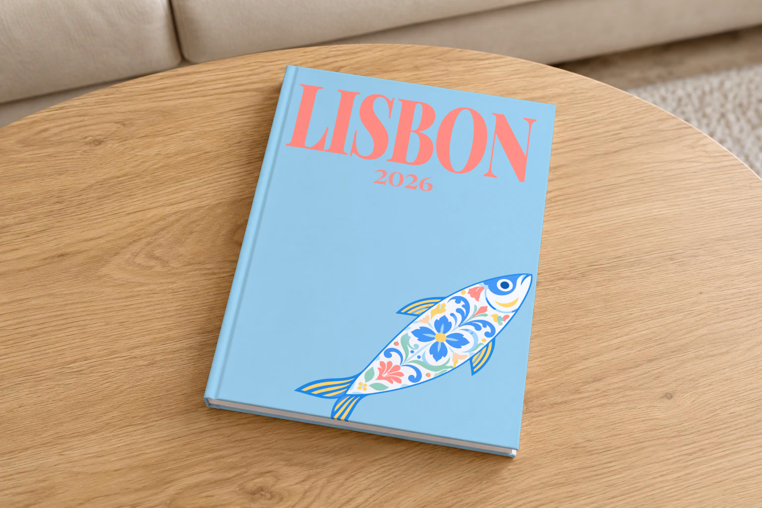 Portugal hardcover photo book with the Lisbon illustrated cover of a leaping azulejo-patterned sardine with pink flowers on pale blue, on a round oak coffee table in a bright living room