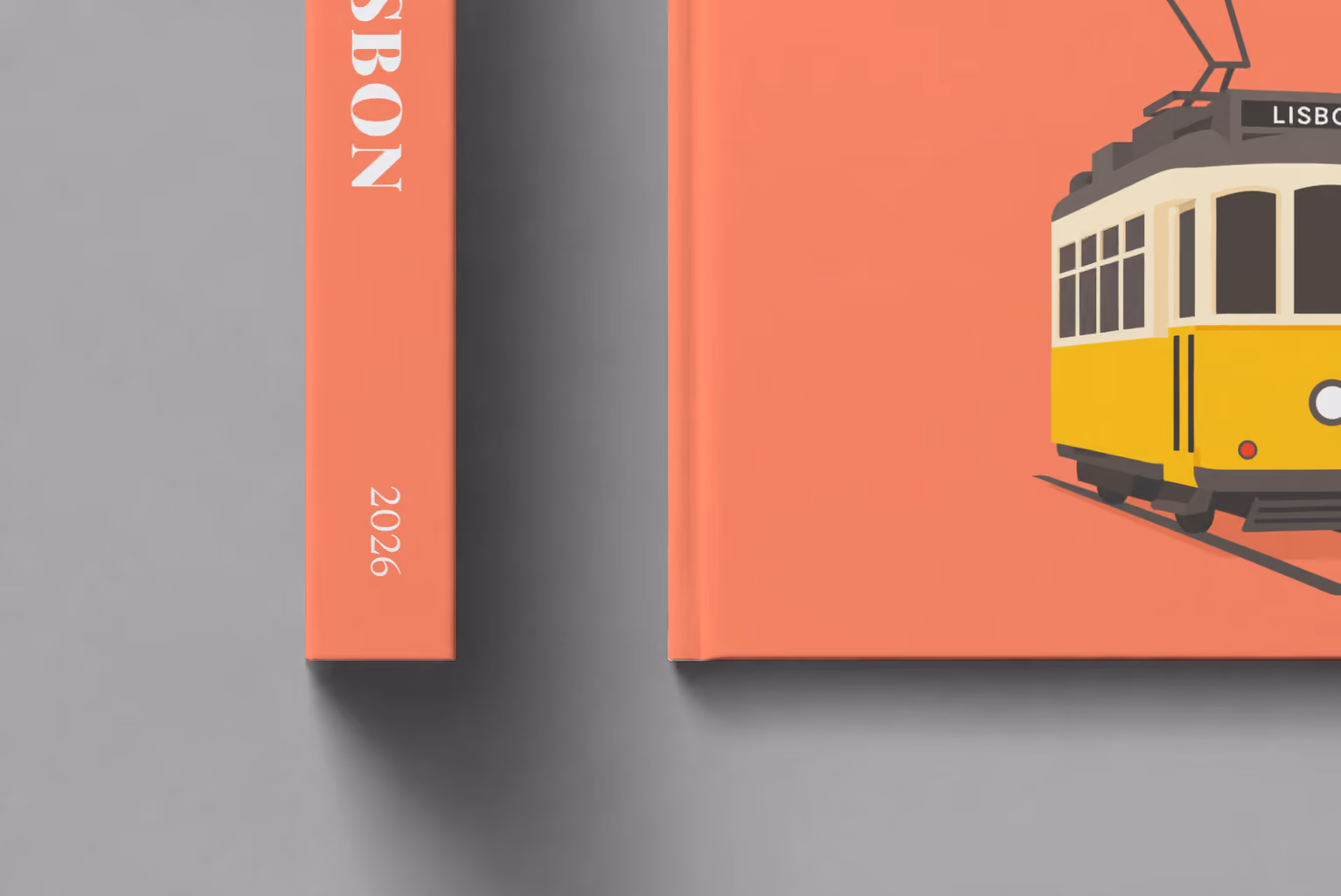 Portugal hardcover photo book with the Lisbon illustrated cover of a yellow vintage Lisbon Tram 28 on coral, shown close up beside its spine on a pale grey studio surface