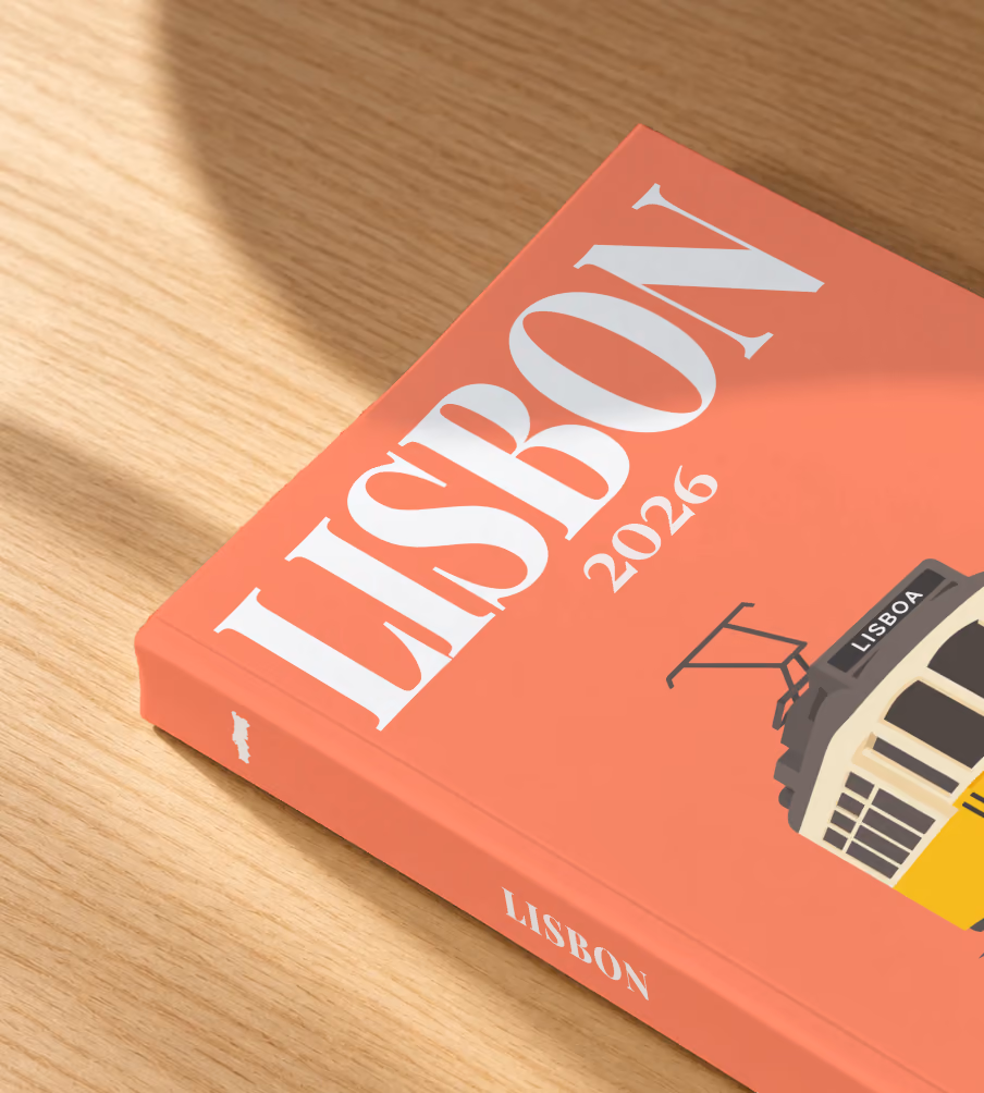 Portugal softcover photo book with the Lisbon illustrated cover of a yellow vintage Lisbon Tram 28 on coral, lying on an oak desk in dappled afternoon sunlight