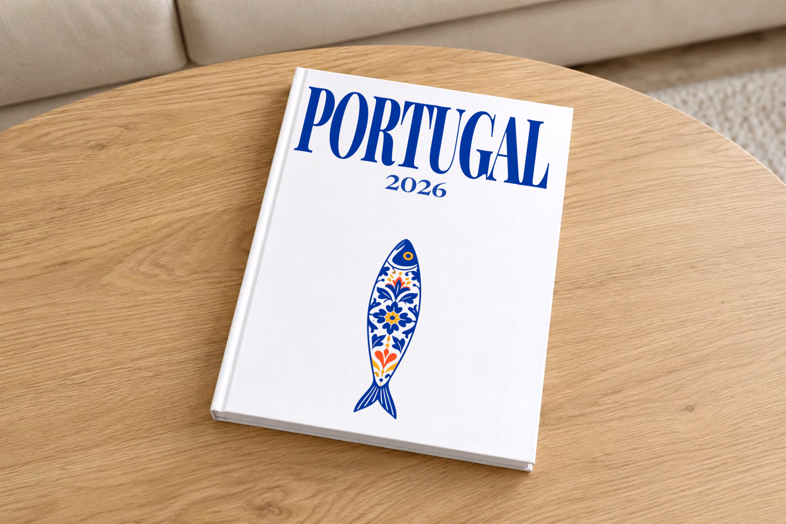 Portugal hardcover photo book with the illustrated cover of a blue and white azulejo-tiled Portuguese sardine on white, on a round oak coffee table in a bright living room