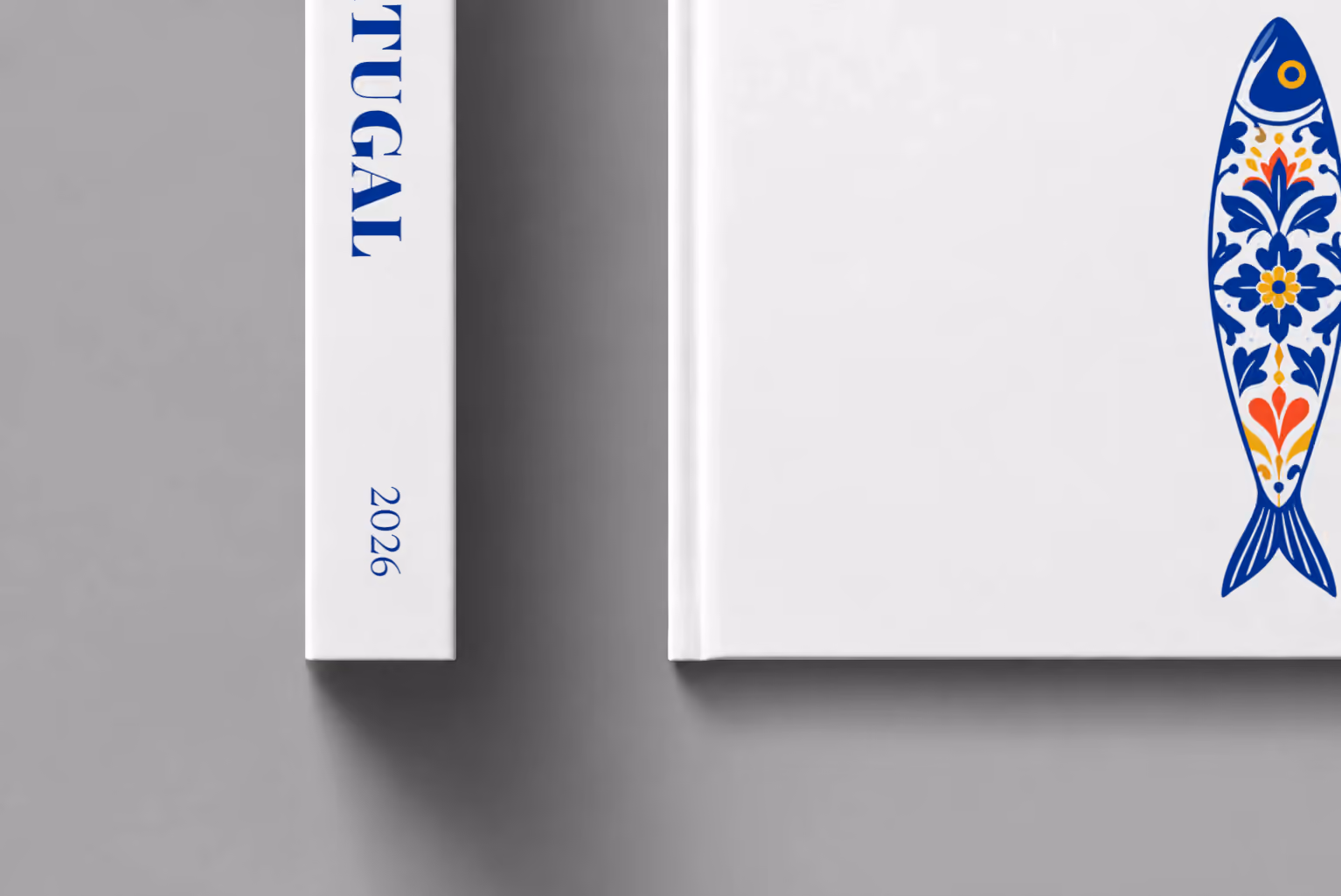 Portugal hardcover photo book with the illustrated cover of a blue and white azulejo-tiled Portuguese sardine on white, shown close up beside its spine on a pale grey studio surface