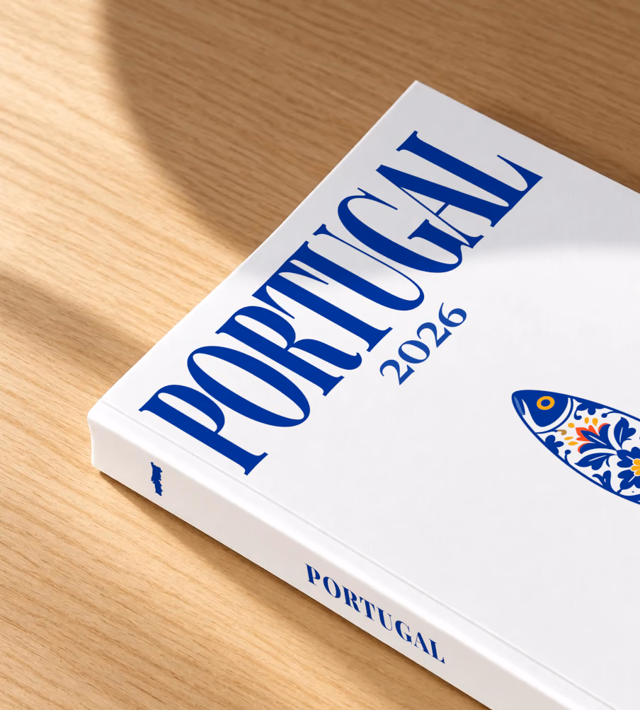 Portugal softcover photo book with the illustrated cover of a blue and white azulejo-tiled Portuguese sardine on white, lying on an oak desk in dappled afternoon sunlight