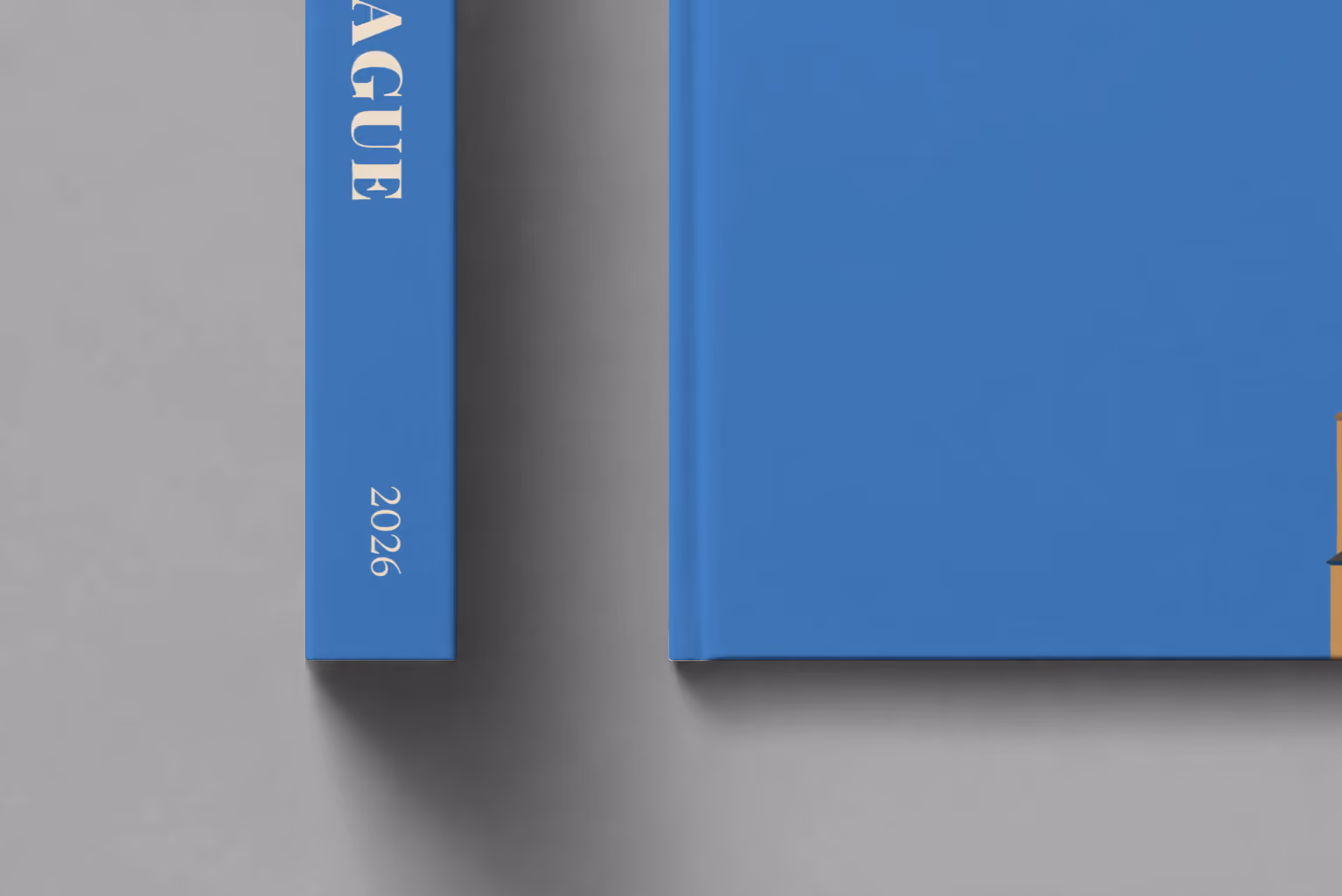 Prague hardcover photo book with the illustrated cover of the Prague Astronomical Clock tower on blue, shown close up beside its spine on a pale grey studio surface