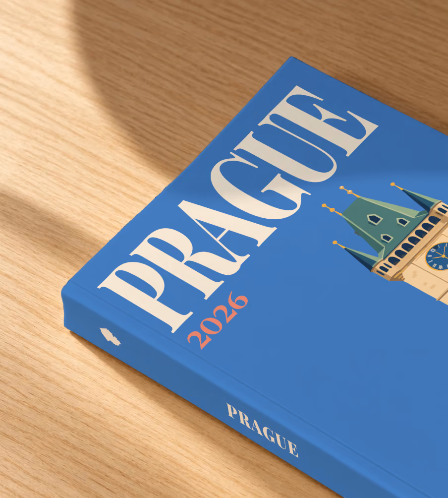 Prague softcover photo book with the illustrated cover of the Prague Astronomical Clock tower on blue, lying on an oak desk in dappled afternoon sunlight