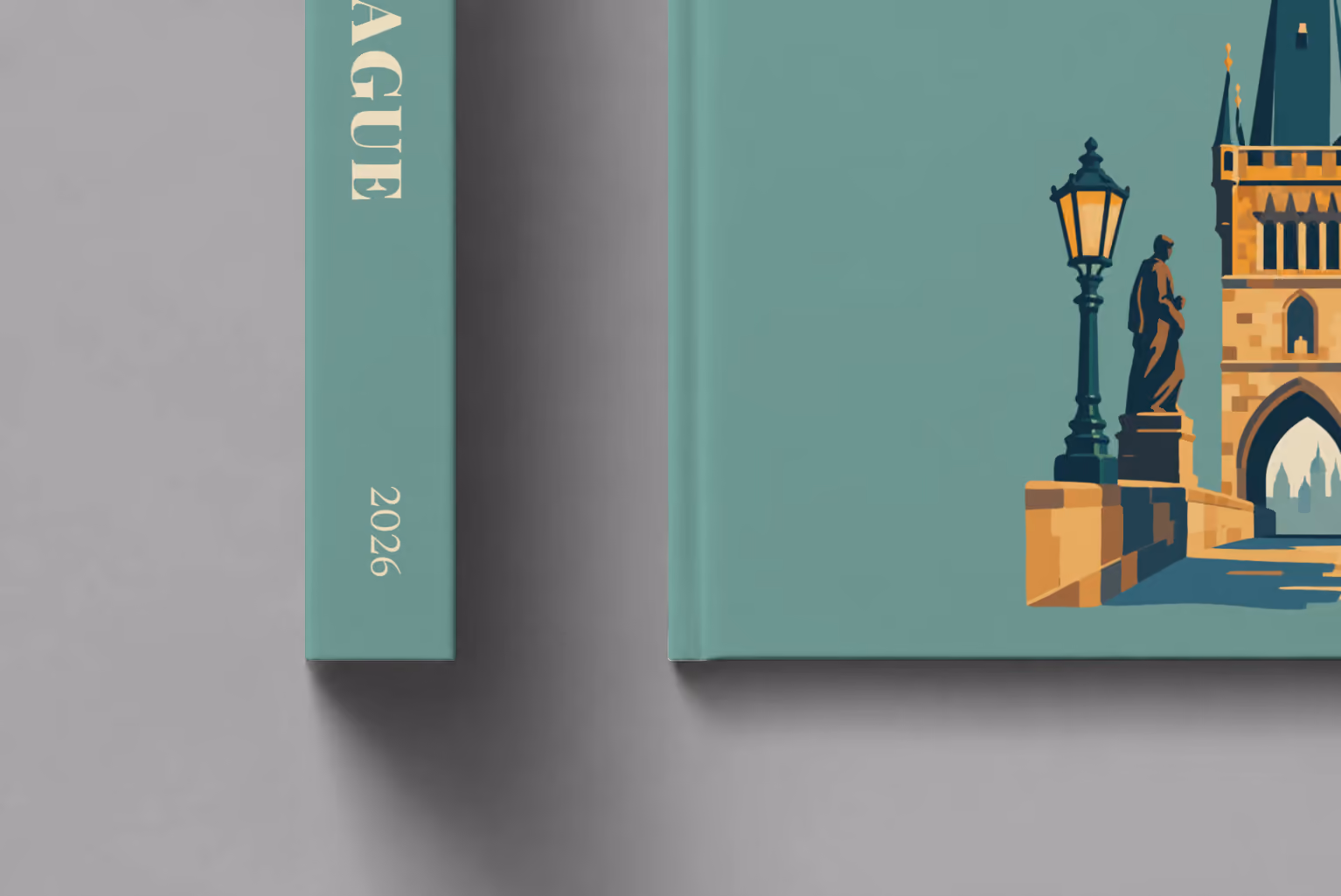 Prague hardcover photo book with the illustrated cover of a Charles Bridge tower with a statue and lamp post on sage green, shown close up beside its spine on a pale grey studio surface