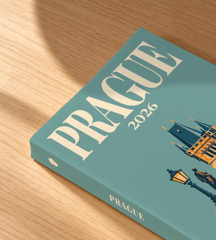 Prague softcover photo book with the illustrated cover of a Charles Bridge tower with a statue and lamp post on sage green, lying on an oak desk in dappled afternoon sunlight