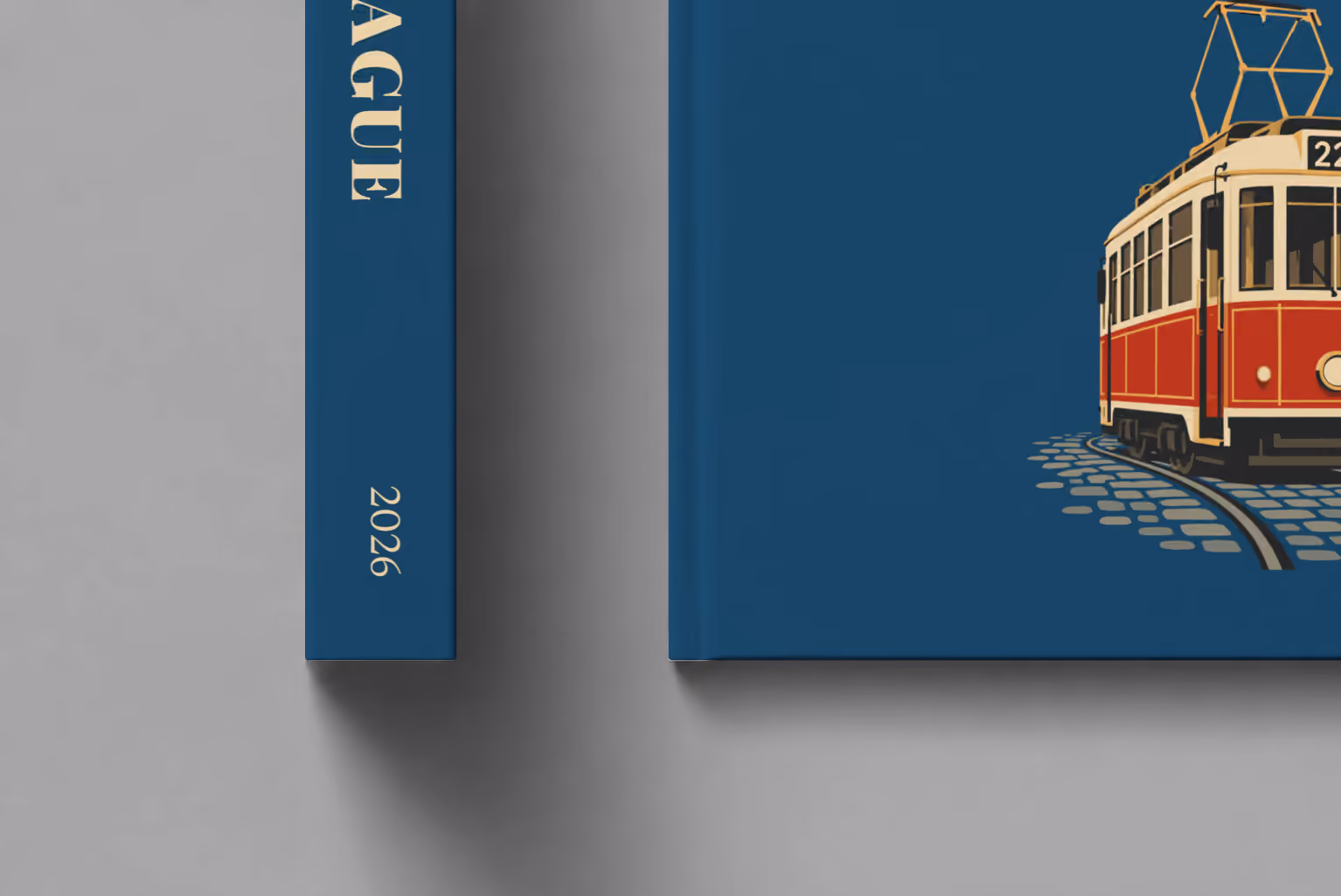 Prague hardcover photo book with the illustrated cover of a red and cream number 22 Prague tram on navy, shown close up beside its spine on a pale grey studio surface