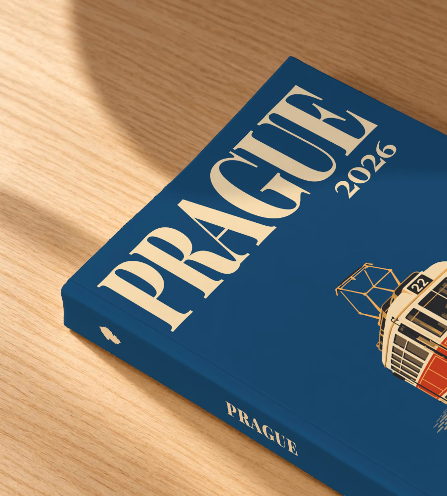 Prague softcover photo book with the illustrated cover of a red and cream number 22 Prague tram on navy, lying on an oak desk in dappled afternoon sunlight