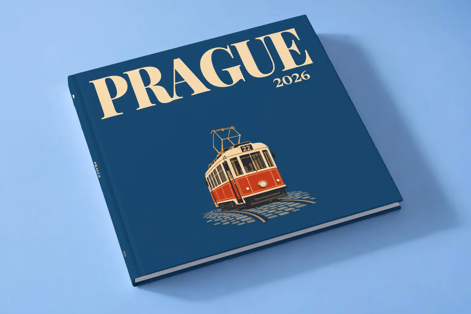 Prague square hardcover photo book with the illustrated cover of a red and cream number 22 Prague tram on navy, lying on a pale blue studio backdrop