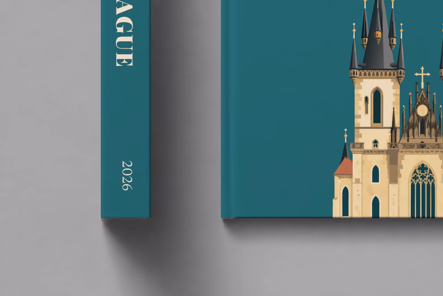 Prague hardcover photo book with the illustrated cover of the Gothic spires of the Church of Our Lady before Týn on teal, shown close up beside its spine on a pale grey studio surface