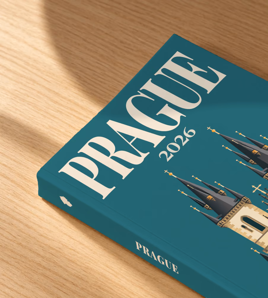 Prague softcover photo book with the illustrated cover of the Gothic spires of the Church of Our Lady before Týn on teal, lying on an oak desk in dappled afternoon sunlight