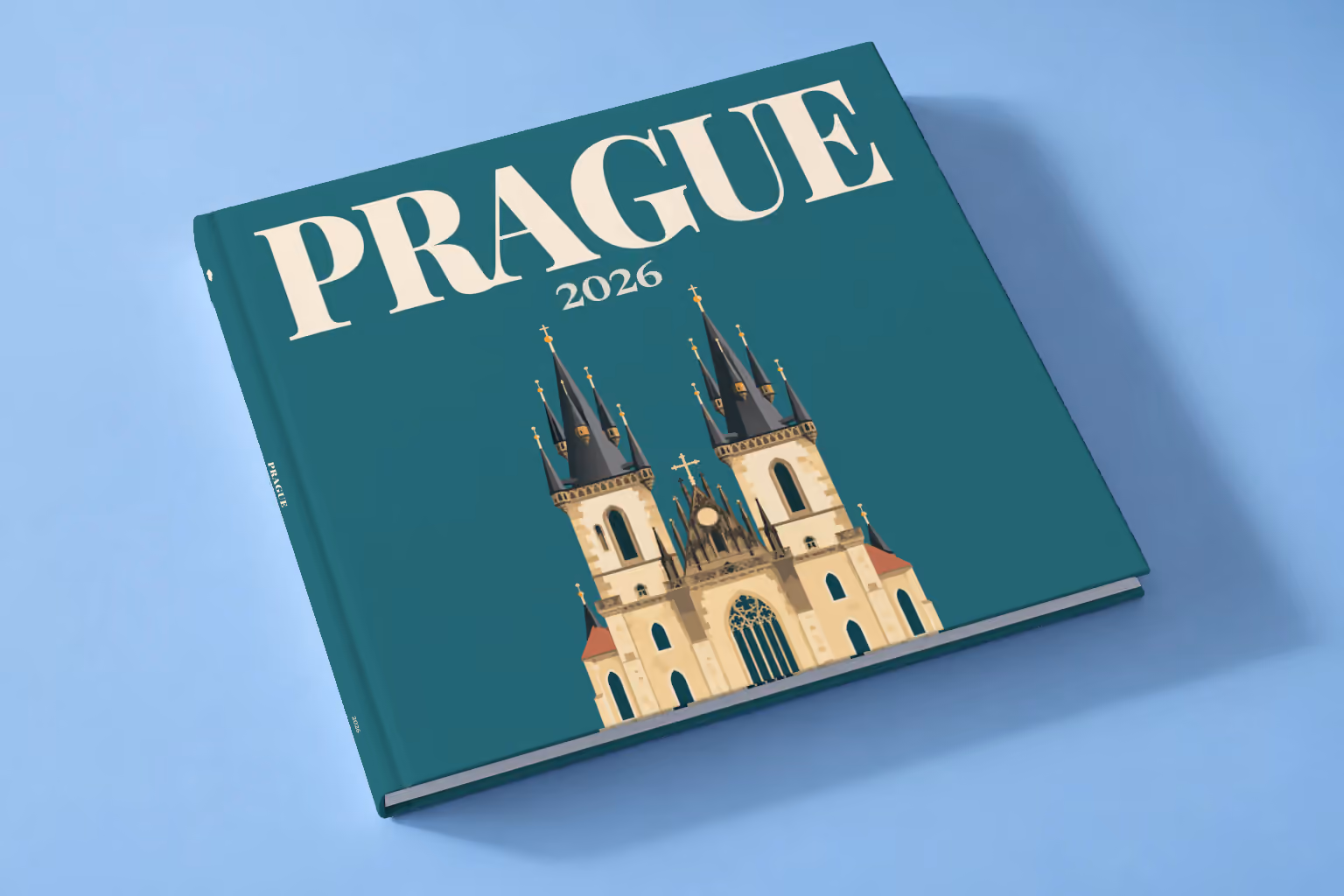 Prague square hardcover photo book with the illustrated cover of the Gothic spires of the Church of Our Lady before Týn on teal, lying on a pale blue studio backdrop