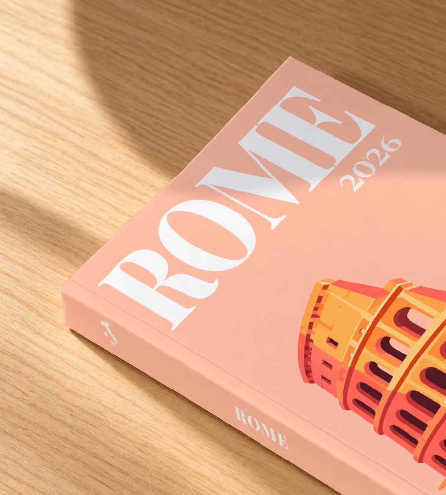 Rome softcover photo book with the illustrated cover of the Colosseum on peach, lying on an oak desk in dappled afternoon sunlight