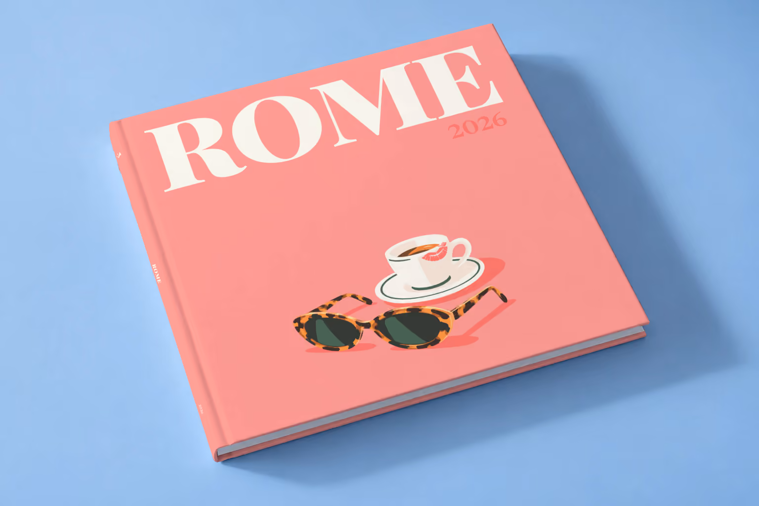 Rome square hardcover photo book with the illustrated cover of an espresso cup and tortoiseshell sunglasses on salmon pink, lying on a pale blue studio backdrop
