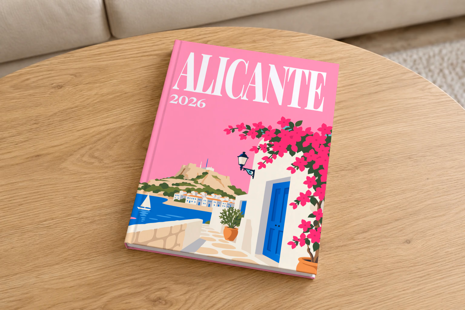 Spain hardcover photo book with the Alicante illustrated cover of a whitewashed street with bougainvillea above the sea on pink, on a round oak coffee table in a bright living room