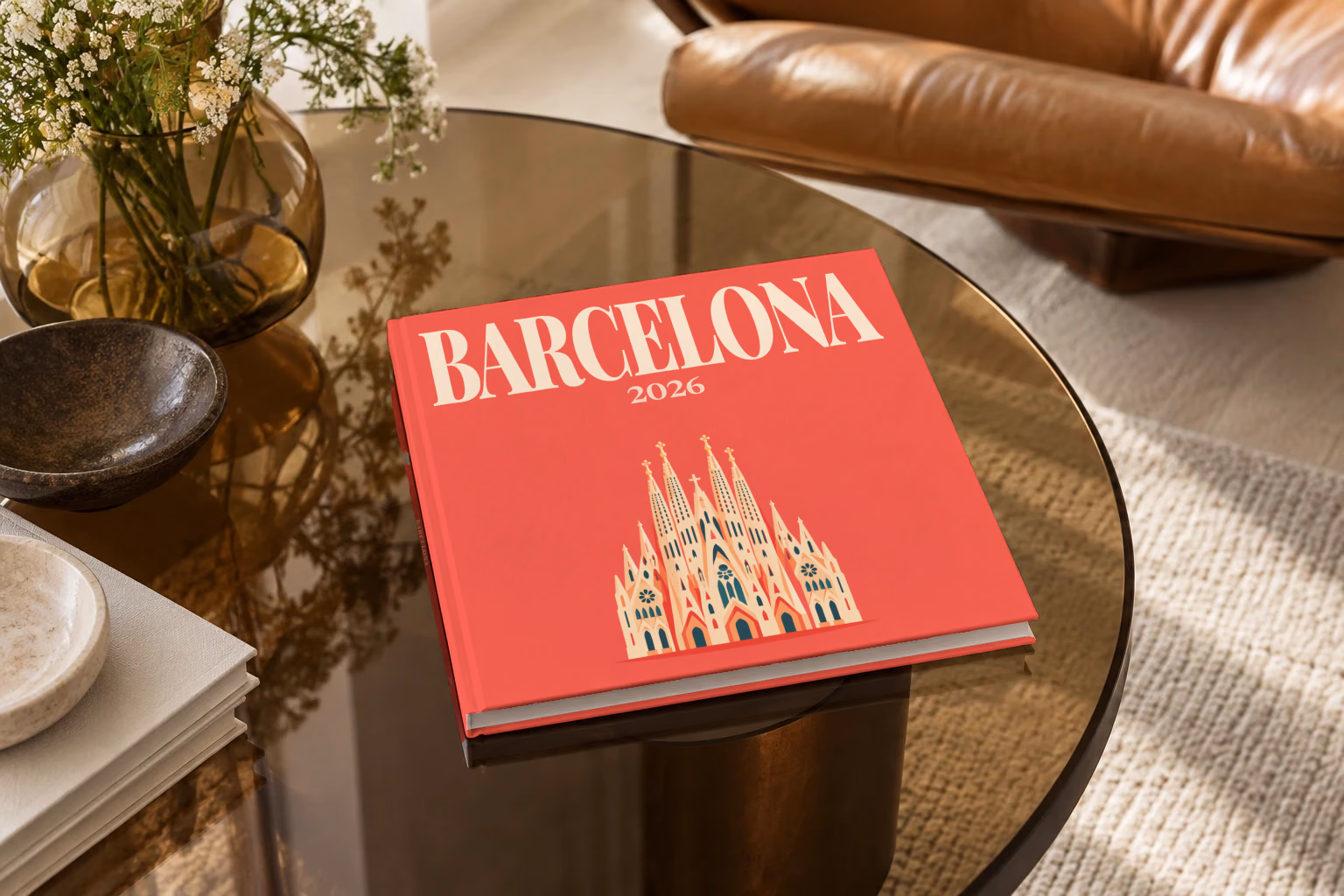 Spain square hardcover photo book with the Barcelona illustrated cover of the Sagrada Família on coral red, on a smoked glass coffee table beside a leather armchair in warm afternoon light