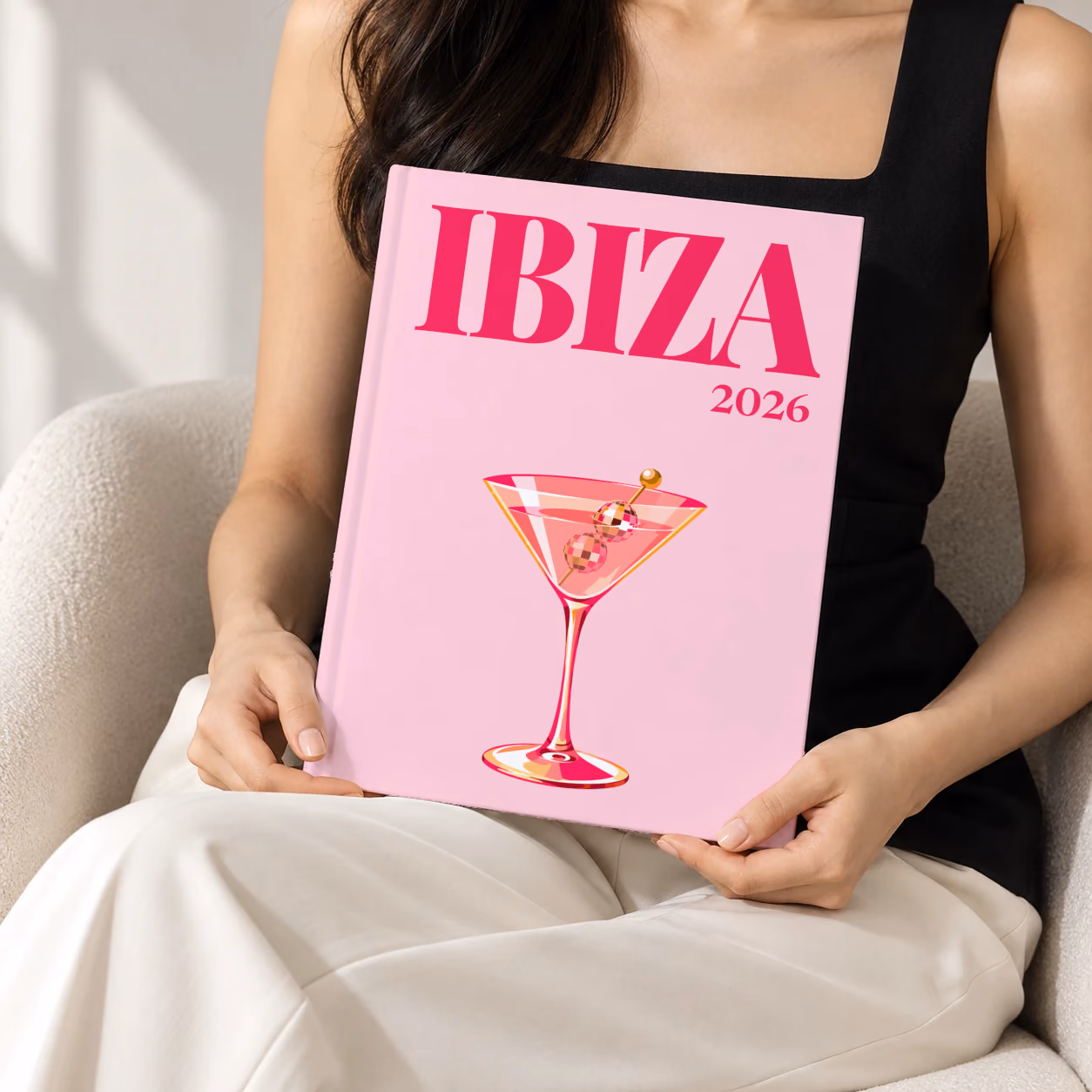 Spain hardcover photo book with the Ibiza illustrated cover of a martini with a disco-ball garnish on pale pink, held upright in two hands by a woman in a black top, sitting in a cream boucle armchair