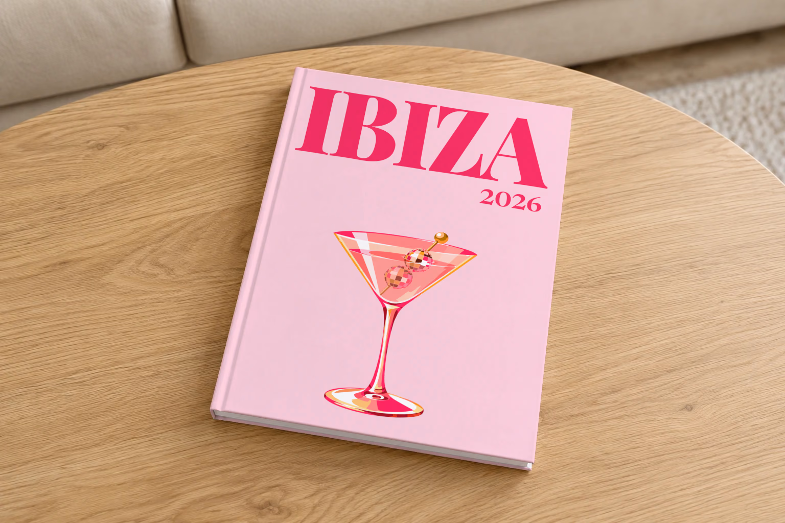 Spain hardcover photo book with the Ibiza illustrated cover of a martini with a disco-ball garnish on pale pink, on a round oak coffee table in a bright living room