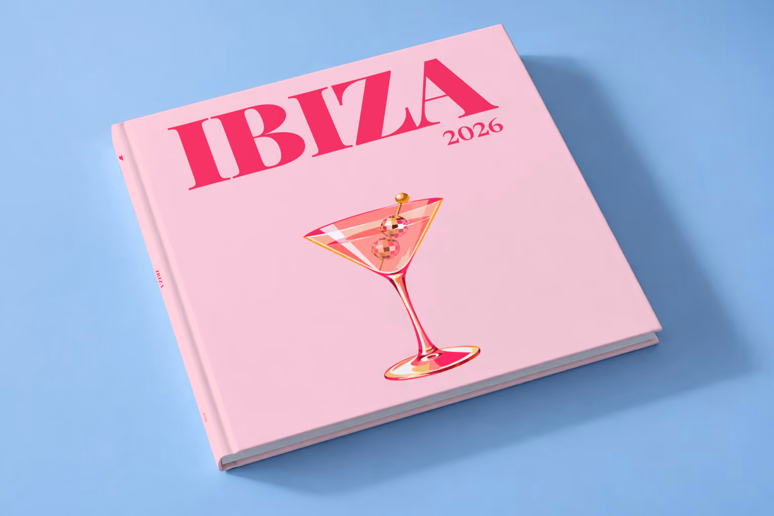 Spain square hardcover photo book with the Ibiza illustrated cover of a martini with a disco-ball garnish on pale pink, lying on a pale blue studio backdrop