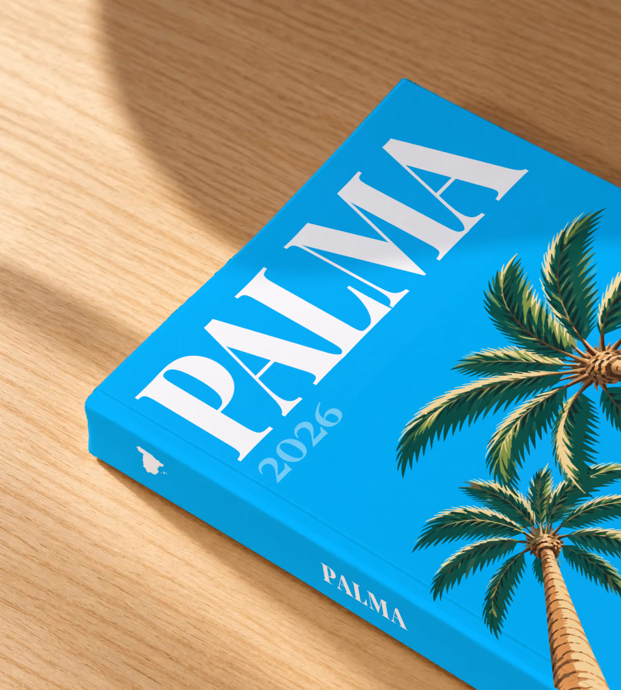 Spain softcover photo book with the Palma illustrated cover of palm trees on bright blue, lying on an oak desk in dappled afternoon sunlight