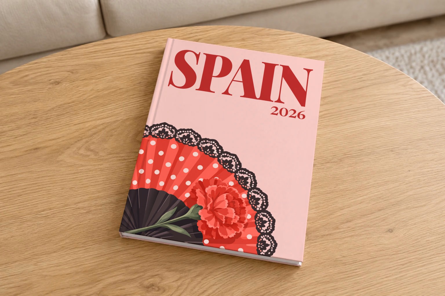 Spain hardcover photo book with the illustrated cover of a polka-dot flamenco fan and a carnation on blush pink, on a round oak coffee table in a bright living room