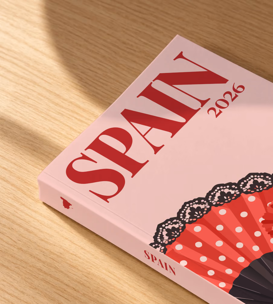 Spain softcover photo book with the illustrated cover of a polka-dot flamenco fan and a carnation on blush pink, lying on an oak desk in dappled afternoon sunlight