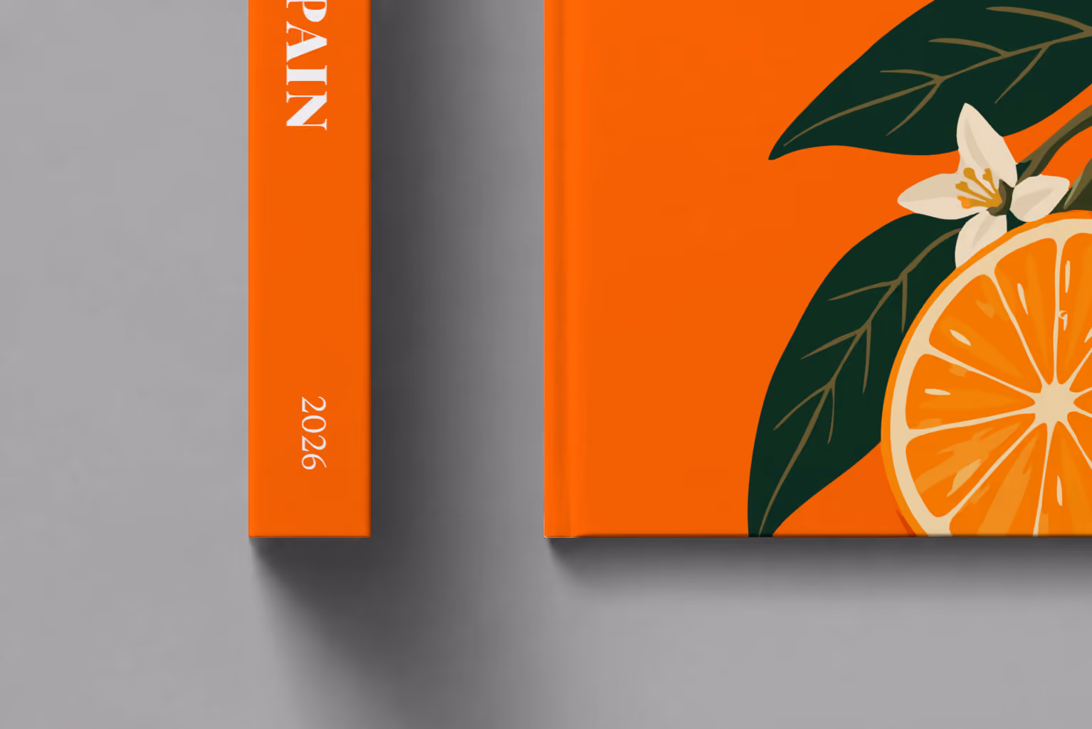 Spain hardcover photo book with the illustrated cover of a halved orange and orange blossom on orange, shown close up beside its spine on a pale grey studio surface