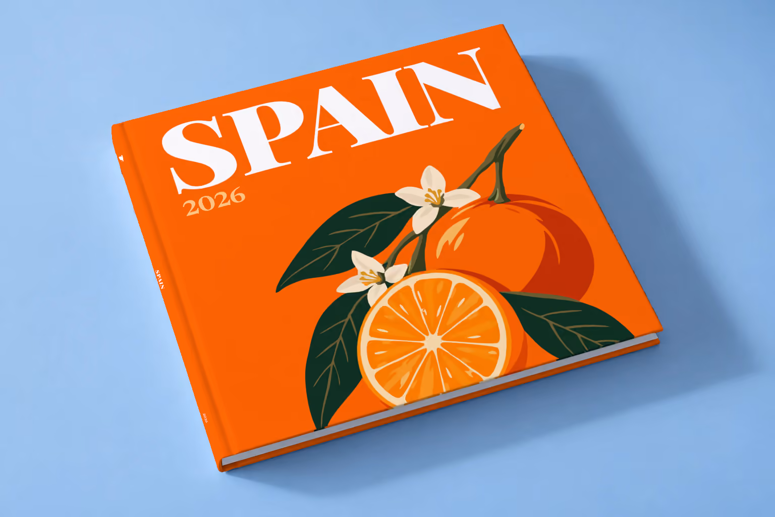 Spain square hardcover photo book with the illustrated cover of a halved orange and orange blossom on orange, lying on a pale blue studio backdrop