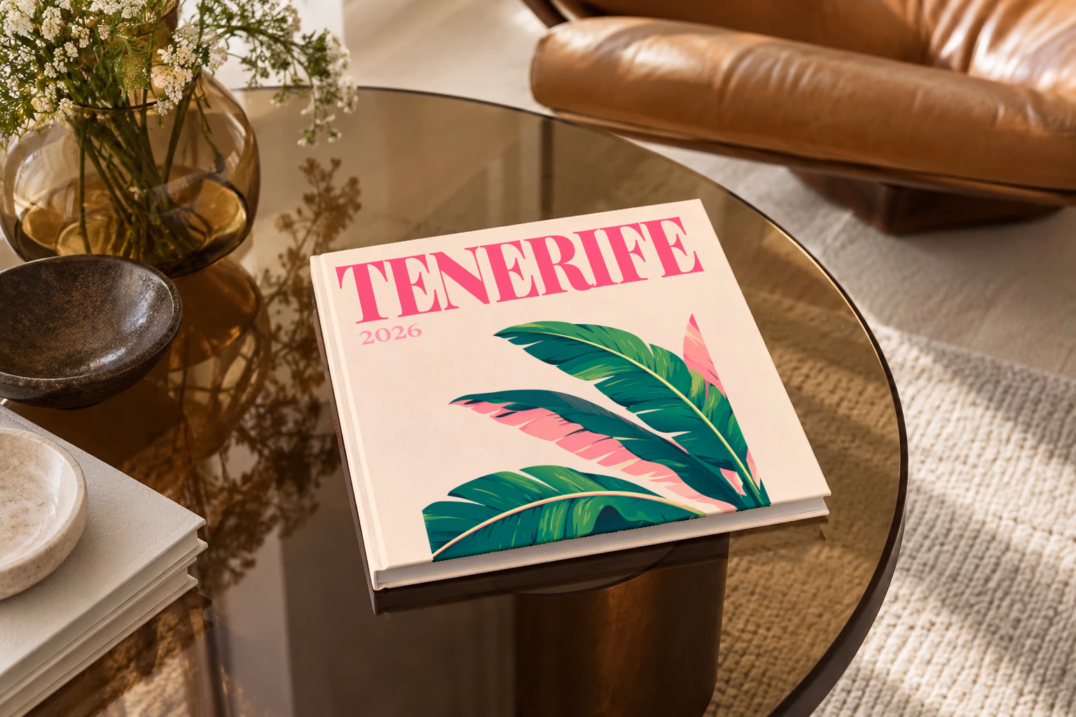 Spain square hardcover photo book with the Tenerife illustrated cover of banana leaves on cream, on a smoked glass coffee table beside a leather armchair in warm afternoon light