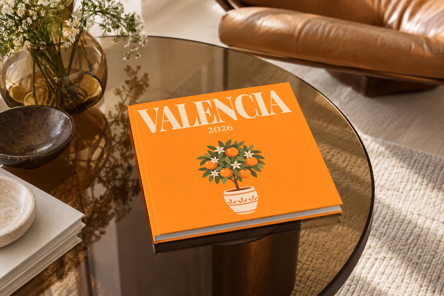 Spain square hardcover photo book with the Valencia illustrated cover of a potted orange tree on orange, on a smoked glass coffee table beside a leather armchair in warm afternoon light