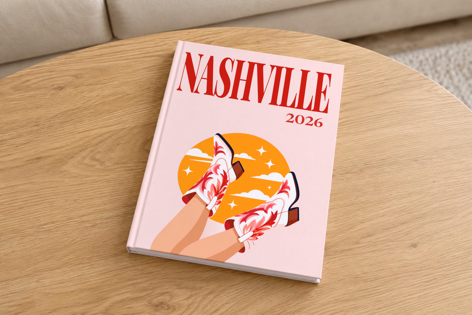 Tennessee hardcover photo book with the Nashville illustrated cover of kicking legs in red and white cowboy boots against a yellow sun on pale pink, on a round oak coffee table in a bright living room