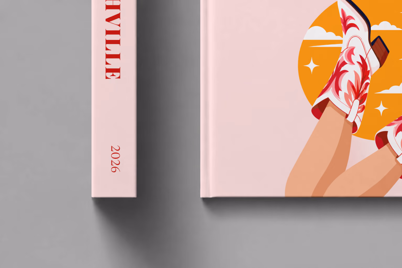 Tennessee hardcover photo book with the Nashville illustrated cover of kicking legs in red and white cowboy boots against a yellow sun on pale pink, shown close up beside its spine on a pale grey studio surface