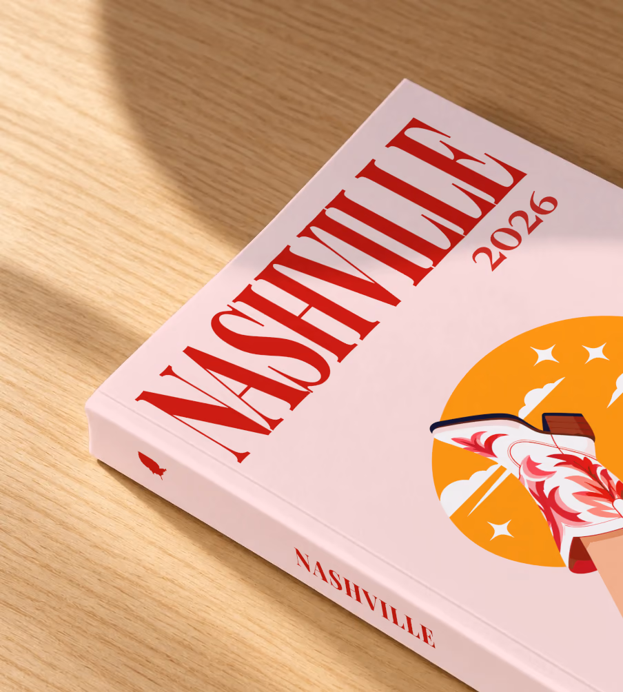 Tennessee softcover photo book with the Nashville illustrated cover of kicking legs in red and white cowboy boots against a yellow sun on pale pink, lying on an oak desk in dappled afternoon sunlight