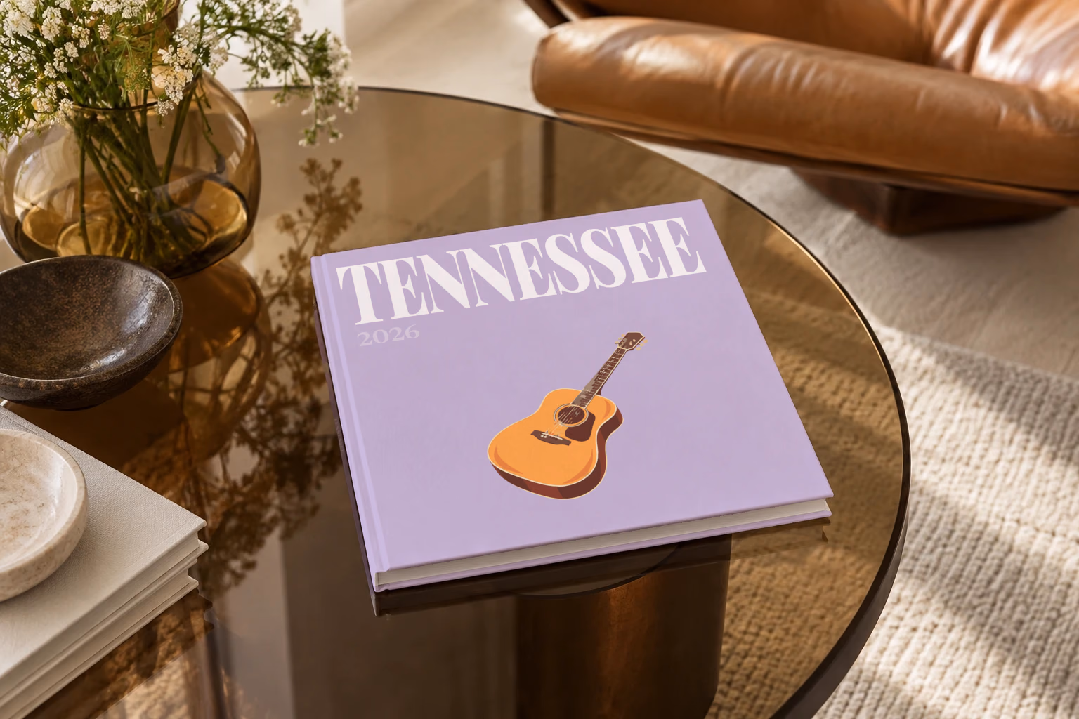 Tennessee square hardcover photo book with the illustrated cover of an acoustic guitar on lilac, on a smoked glass coffee table beside a leather armchair in warm afternoon light