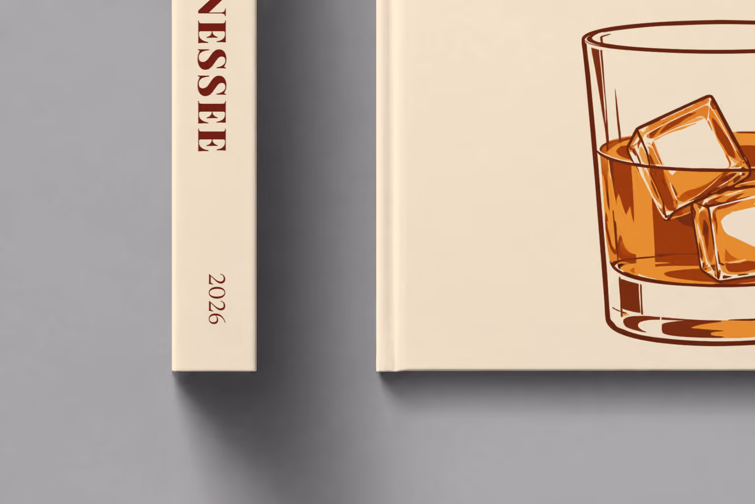 Tennessee hardcover photo book with the illustrated cover of a glass of Tennessee whiskey on the rocks on pale apricot, shown close up beside its spine on a pale grey studio surface