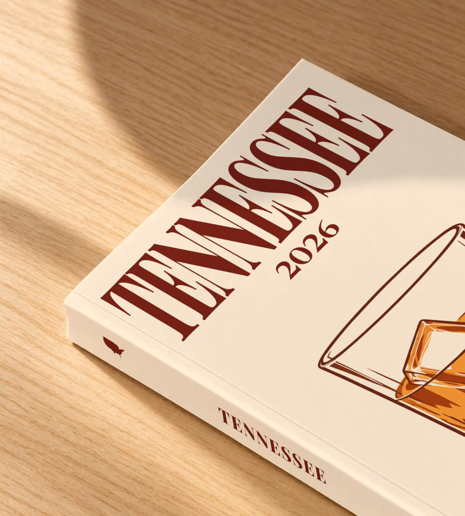 Tennessee softcover photo book with the illustrated cover of a glass of Tennessee whiskey on the rocks on pale apricot, lying on an oak desk in dappled afternoon sunlight