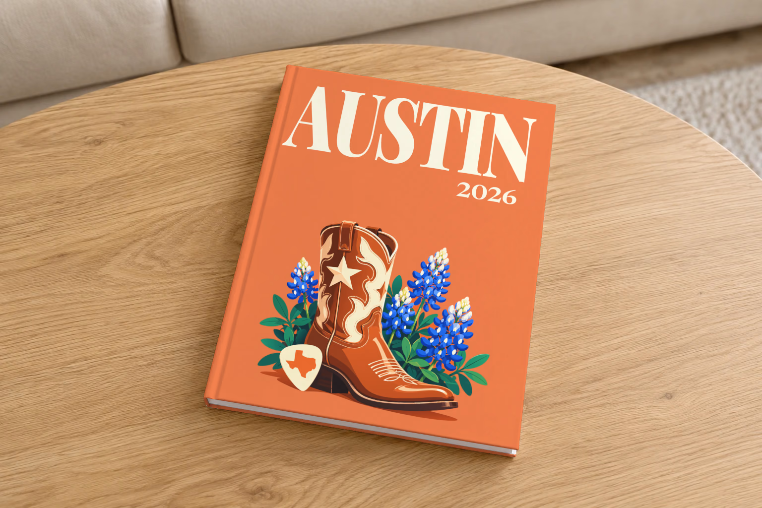 Texas hardcover photo book with the Austin illustrated cover of a cowboy boot with Texas bluebonnets and a guitar pick on coral, on a round oak coffee table in a bright living room