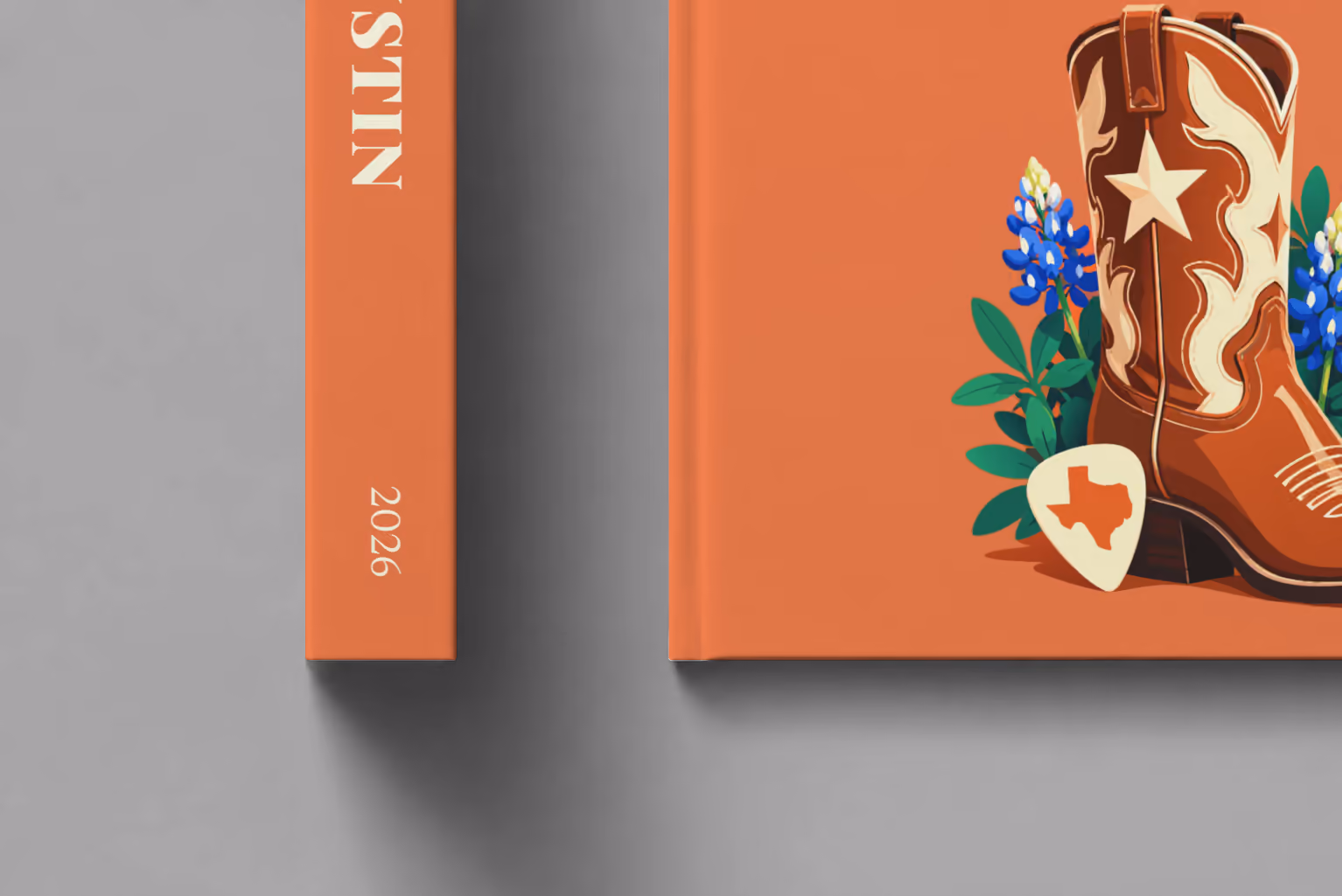 Texas hardcover photo book with the Austin illustrated cover of a cowboy boot with Texas bluebonnets and a guitar pick on coral, shown close up beside its spine on a pale grey studio surface