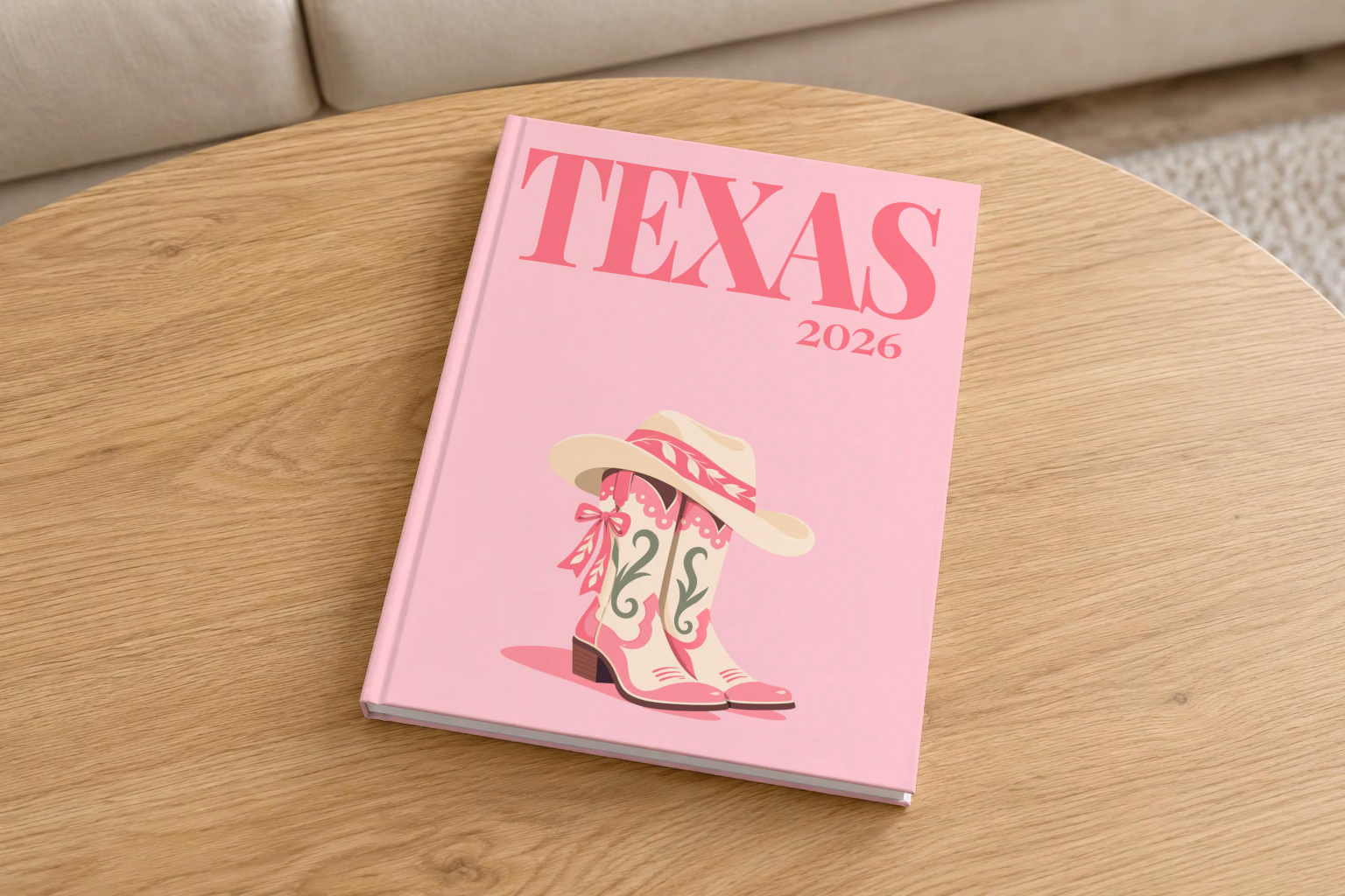 Texas hardcover photo book with the illustrated cover of pink cowboy boots with bows and a cowboy hat on blush pink, on a round oak coffee table in a bright living room