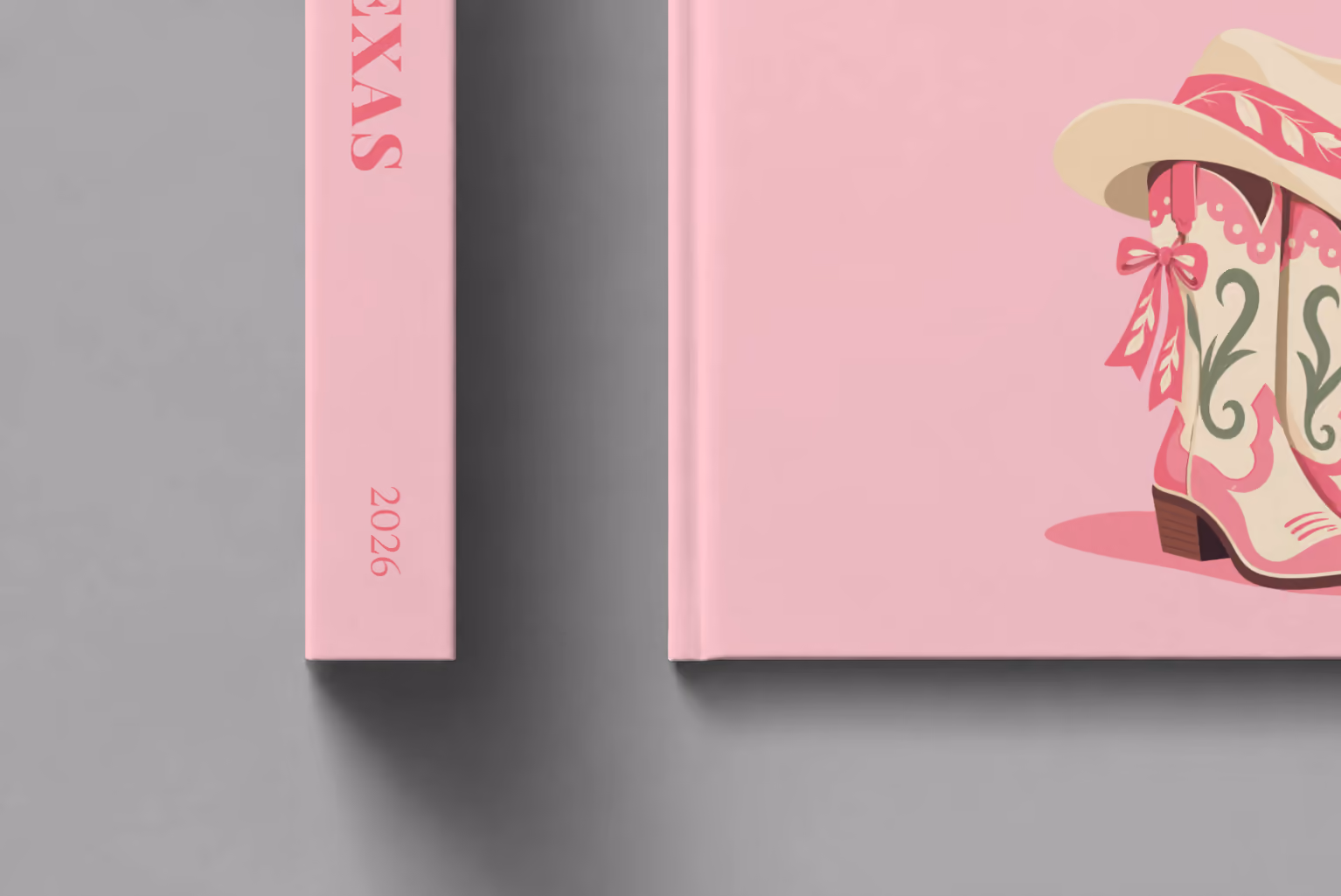 Texas hardcover photo book with the illustrated cover of pink cowboy boots with bows and a cowboy hat on blush pink, shown close up beside its spine on a pale grey studio surface