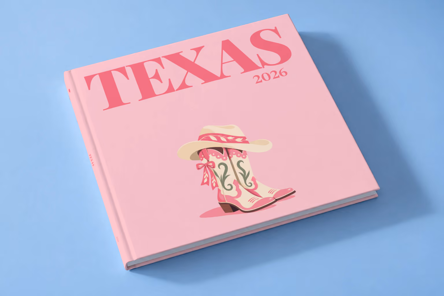 Texas square hardcover photo book with the illustrated cover of pink cowboy boots with bows and a cowboy hat on blush pink, lying on a pale blue studio backdrop