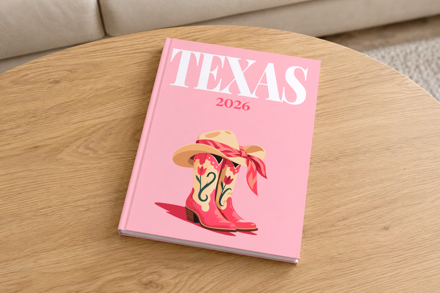 Texas hardcover photo book with the illustrated cover of pink cowboy boots and a cowboy hat with a pink bandana on pink, on a round oak coffee table in a bright living room